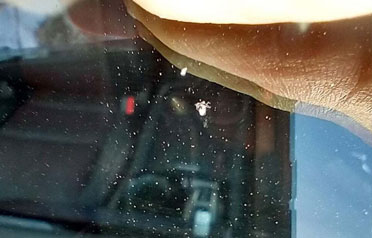 Tiny windshield chip under close inspection with hand shadow visible on glass surface